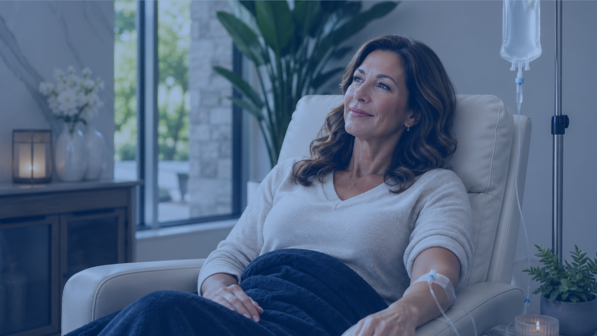 Woman relaxing under a blanket in a recliner while receiving an IV drip in a calm spa room